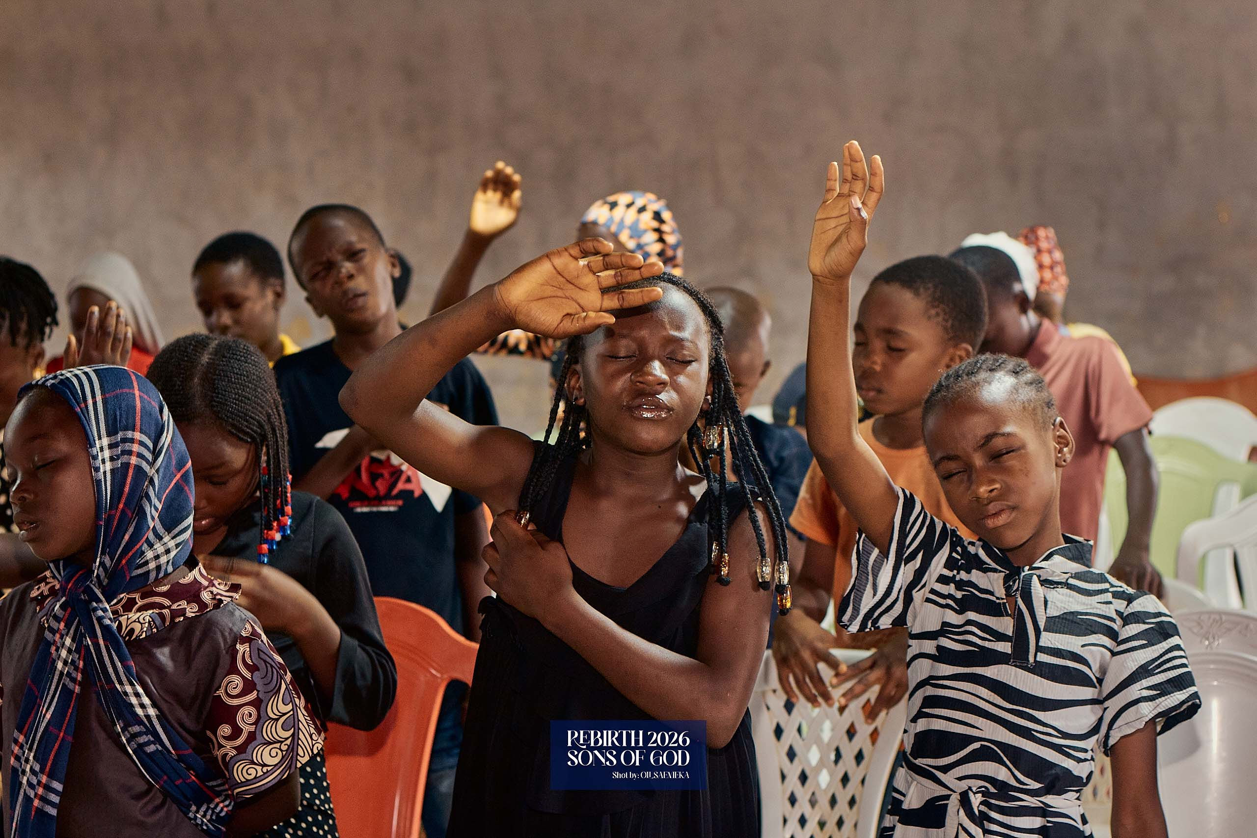 Children gathered indoors with several hands raised.