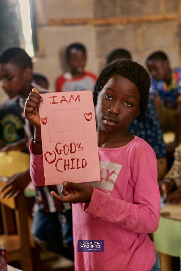 A child displaying a pink handmade card that reads I am God's child.
