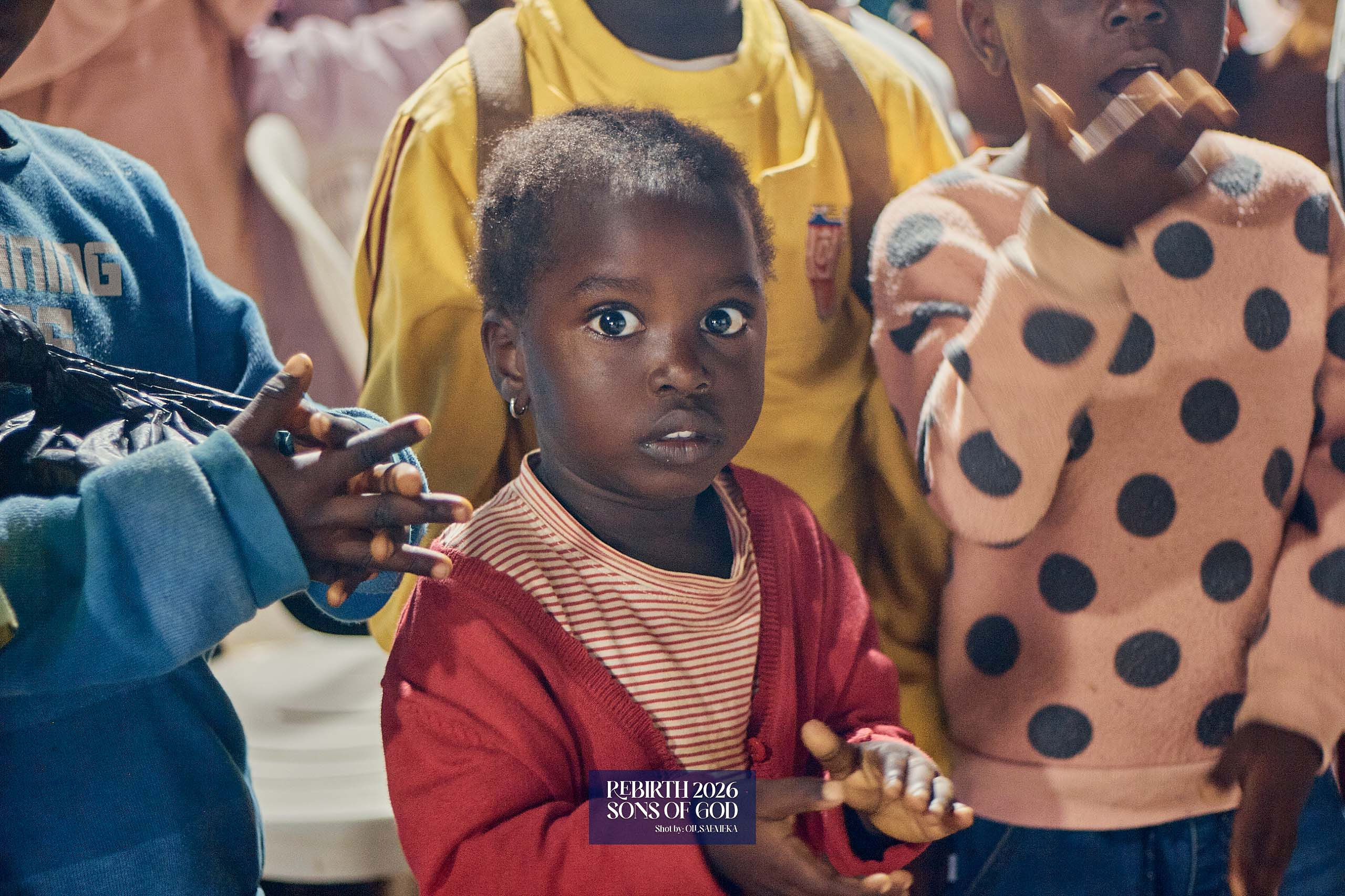 A young child standing among other children indoors.