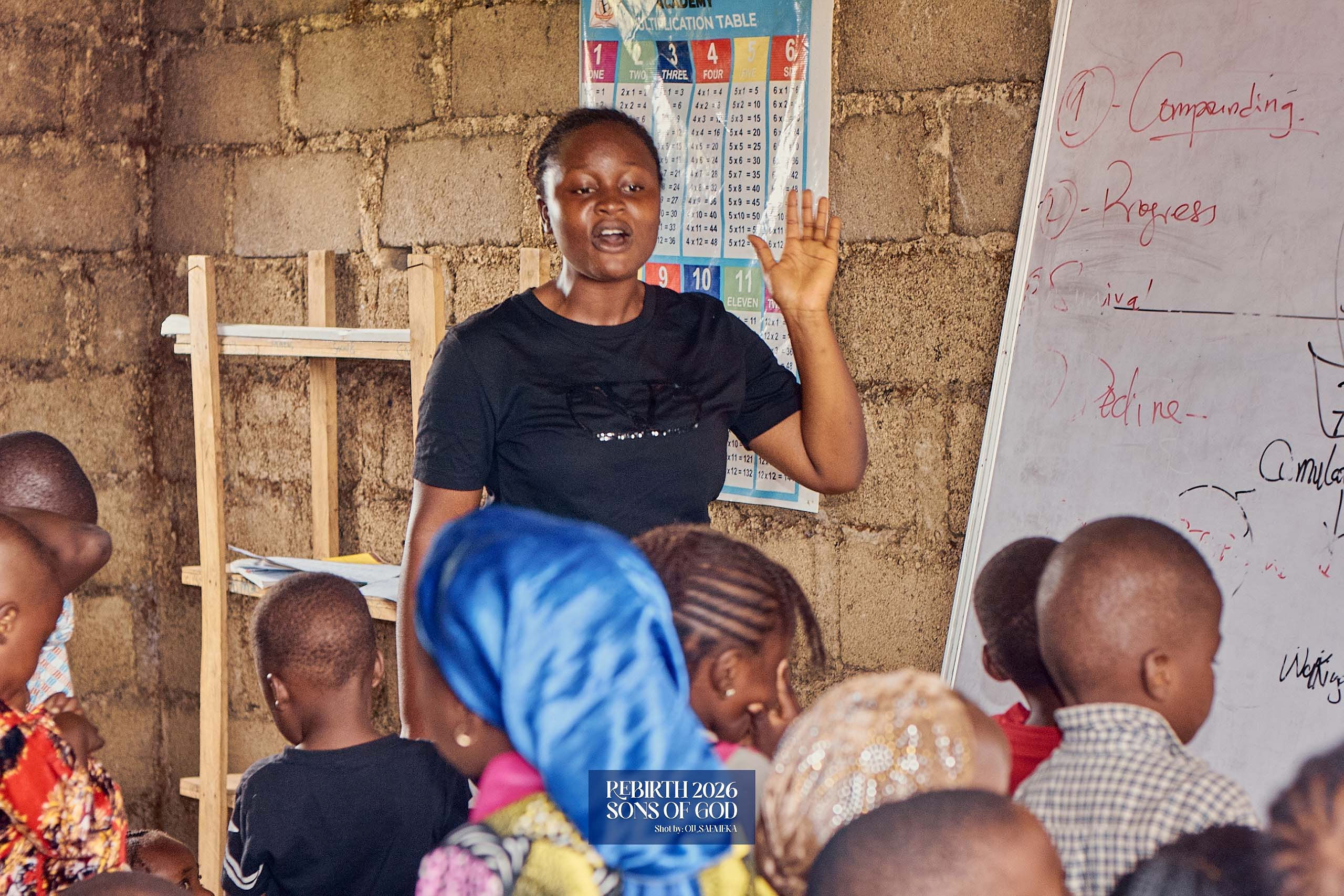A teacher speaking to children in front of a whiteboard.